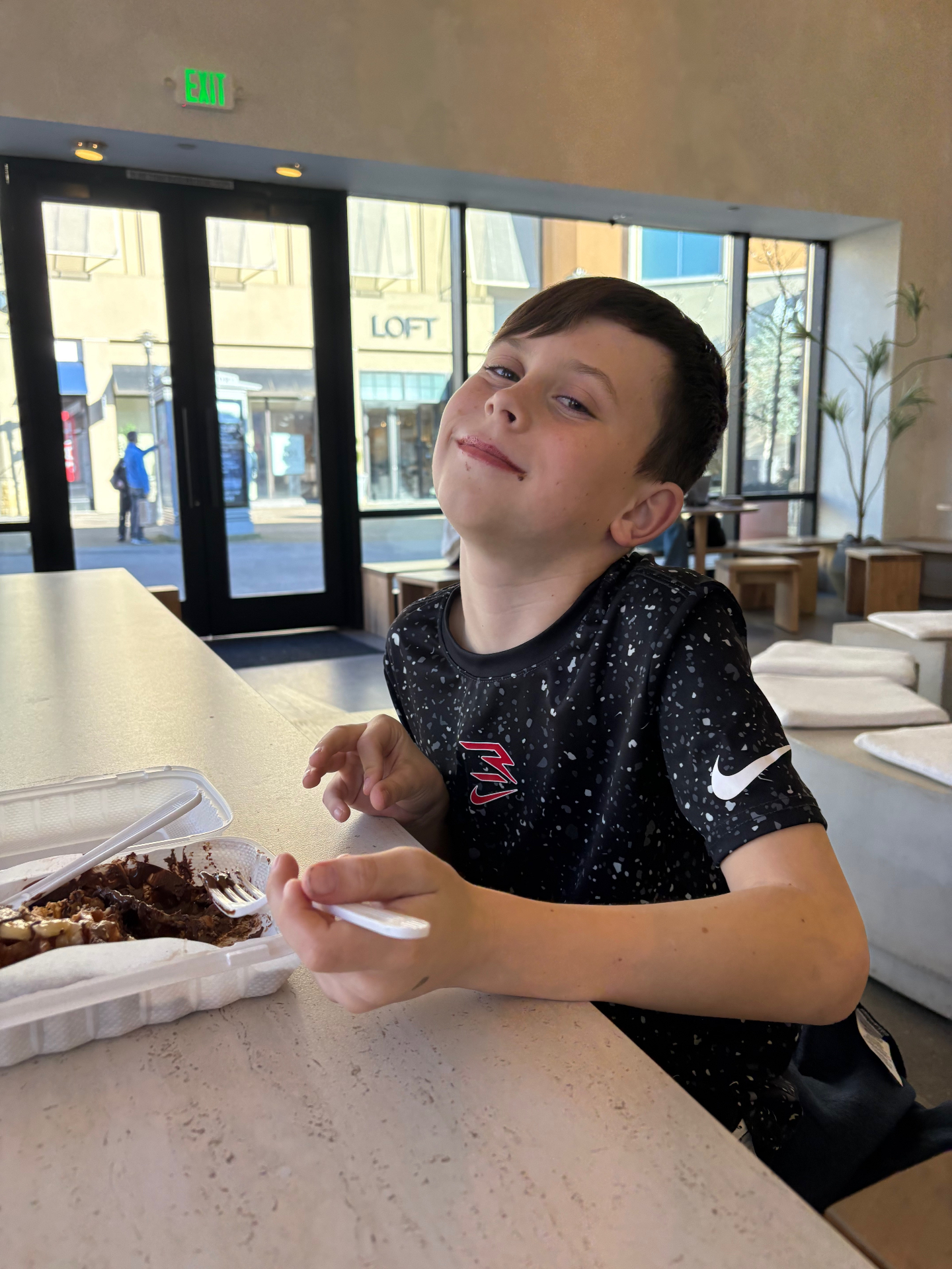 Older son grinning across a cafe table after a chocolate dessert.